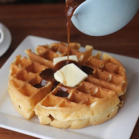 Waffle on a plate with butter and syrup being poured on