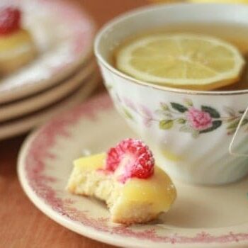 Lemon Curd and Raspberry Tea Cookie on a plate with a bite taken out beside a cup of tea