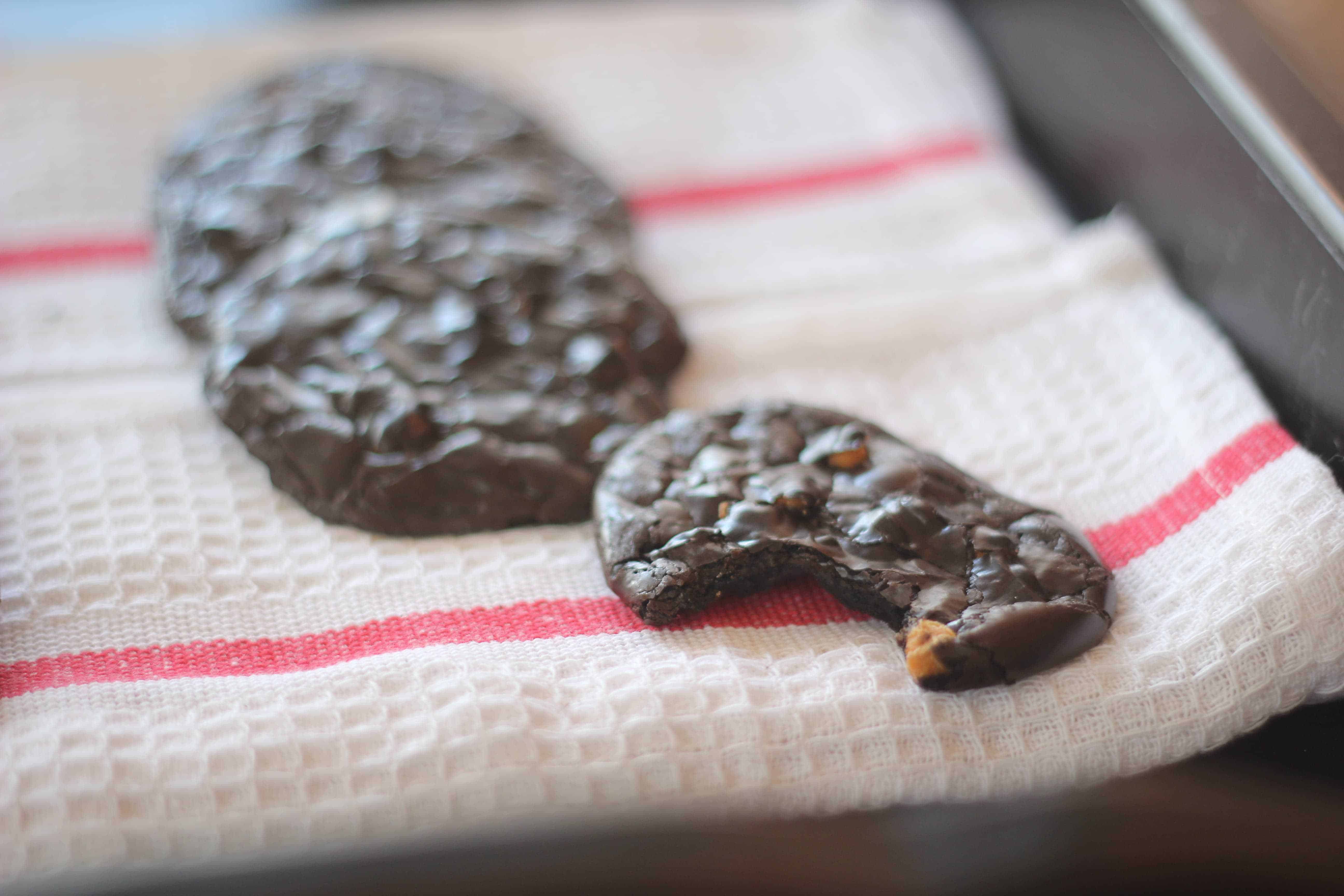 Flourless Dark Chocolate Espresso Cookies with Butterscotch Chips on a tea towel with a bite taken out