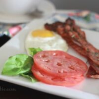 Perfectly Crisp Rosemary Pepper Bacon on a plate with a fried egg and tomato slices