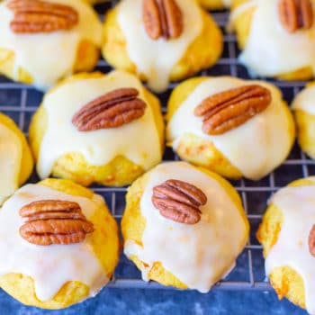 Carrot cookies with orange icing lined up and topped with a pecan halve