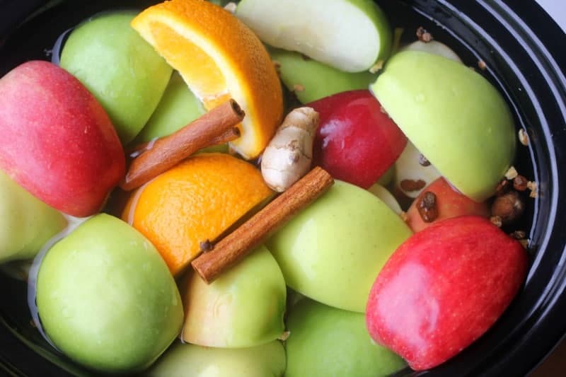 Apple and orange slices, cinnamon stick and other spices in the crockpot before being cooked