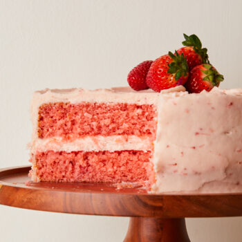 strawberry cake on a cake plate with a slice taken out