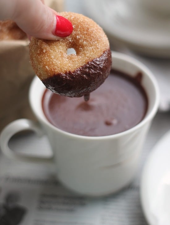 A mini baked donut being dunked in a cup of melted chocolate 