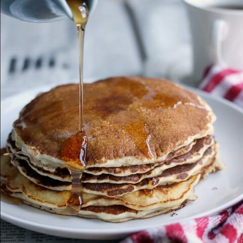 Pancakes stacked on a plate with syrup being poured on