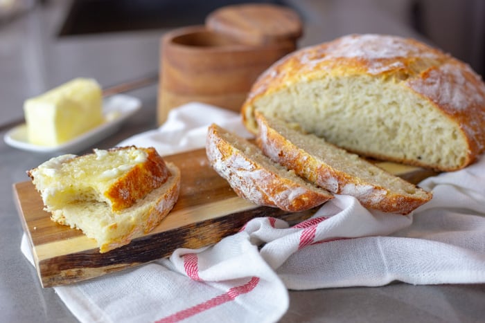 dutch oven bread sliced on a cutting board with butter