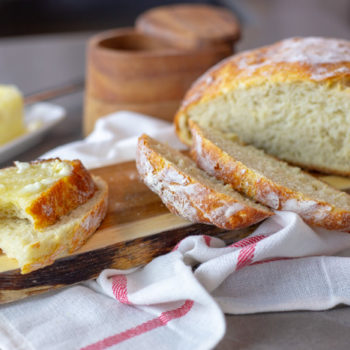 Rustic Bread sliced on a cutting board with butter on the side