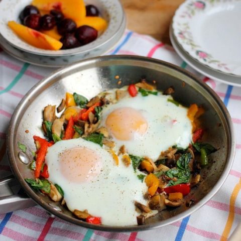 Roasted veggies in a skillet topped with over-easy eggs