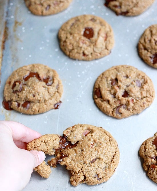 Chocolate chip cookies on a baking sheet with a piece being torn off one cookie