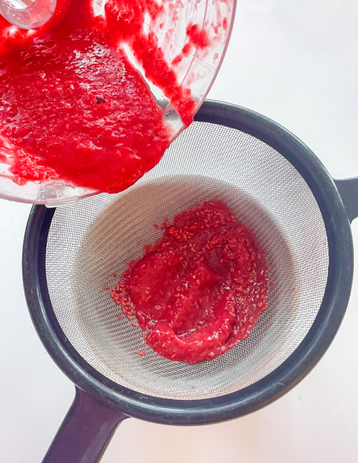 pushing pureed raspberries through a mesh sieve