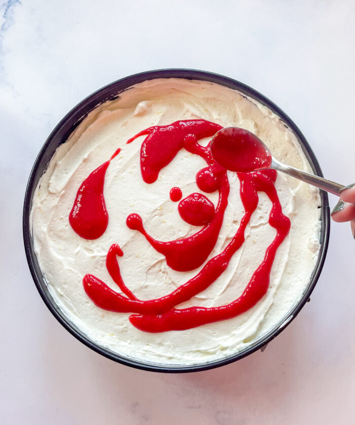raspberry puree being spread over the cheesecake filling