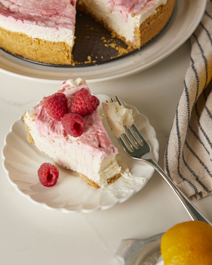a slice of lemon raspberry cheesecake on a plate with a bite taken out