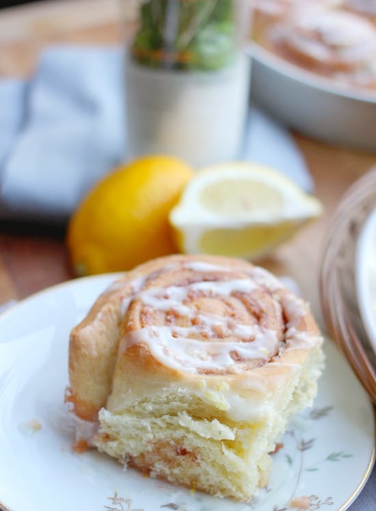 A Rosemary Lemon Cinnamon Rolls on a plate drizzled with glaze