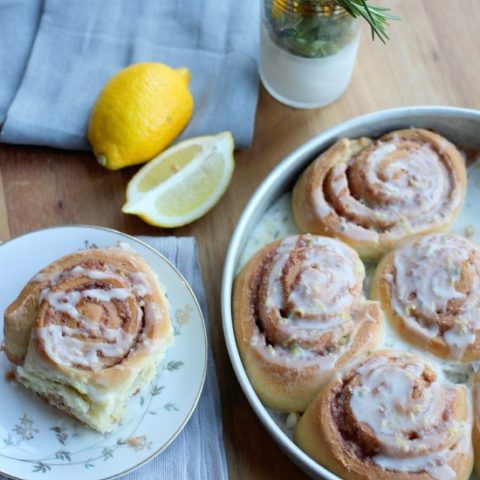 A Rosemary Lemon Cinnamon Rolls on a plate drizzled with glaze