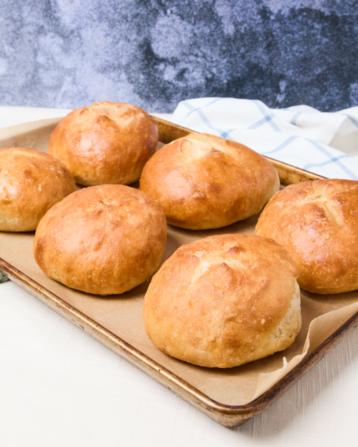 Homemade bread bowls on a sheet pan after baking and before the tops are cut off and filled.