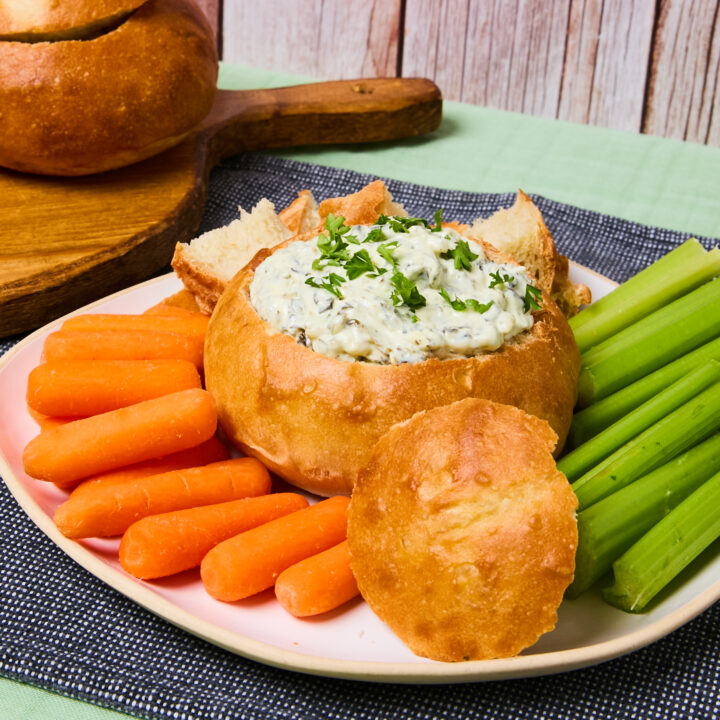 Homemade bread bowl filled with spinach dip and surrounded by baby carrots and celery