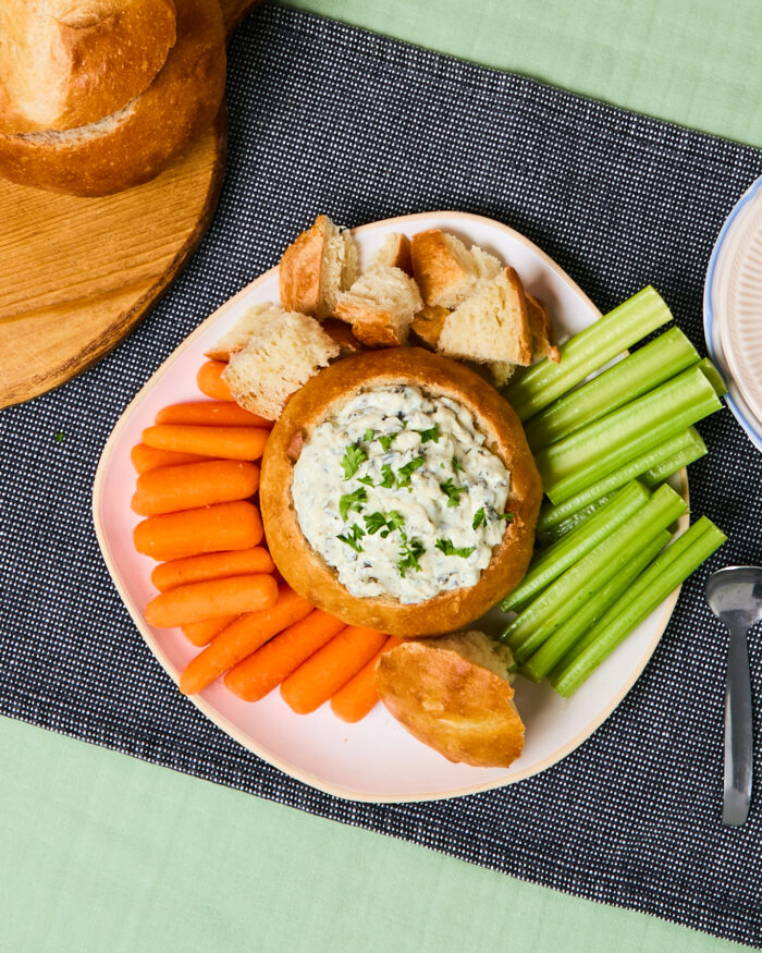 Homemade bread bowl filled with spinach dip and surrounded by baby carrots and celery