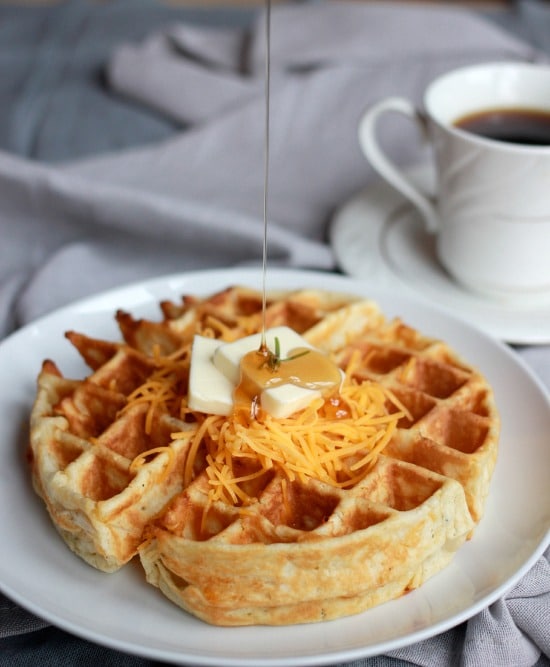 Cheddar and Rosemary waffle with shredded cheddar, pad of butter and syrup on top