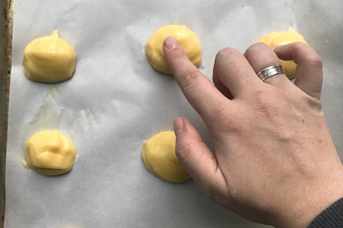 My finger pressing down the tips of the raw choux rounds