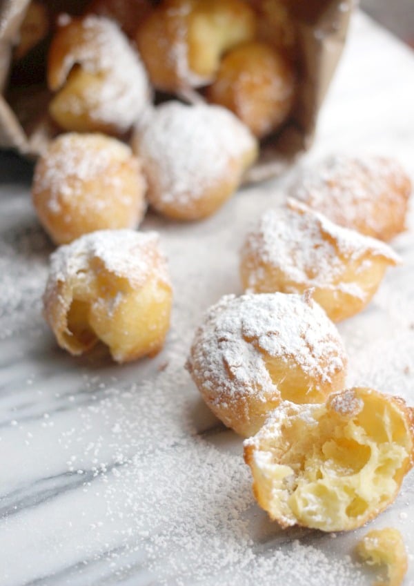 Pate a Choux Beignets spilled out of a paper bag sprinkled with powdered sugar