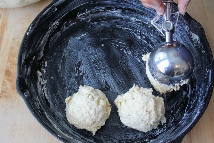 Scooping drop biscuits into a greased cast iron pan.