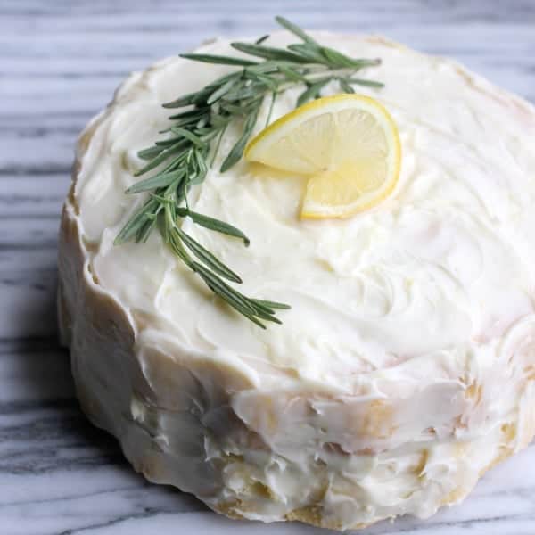 Fluffy Lemon-Rosemary Layer Cake with Lemon Cream Cheese Frosting with a sprig of rosemary and lemon wedge as decoration on top