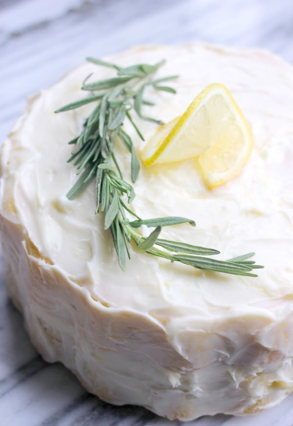 Fluffy Lemon-Rosemary Layer Cake with Lemon Cream Cheese Frosting with a sprig of rosemary and lemon wedge as decoration on top