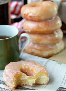 Stacked glazed donuts with cup of coffee and newspaper