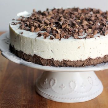 Easy No-Bake Cheesecake on a cake stand topped with peanut butter cups and shaved chocolate