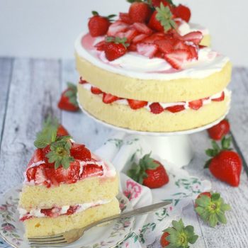 Lemon Strawberry Cream Cake on a cake stand with a slice cut out