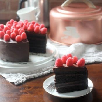 A slice of Devils Food Cake with Ganache Frosting and topped with fresh raspberries