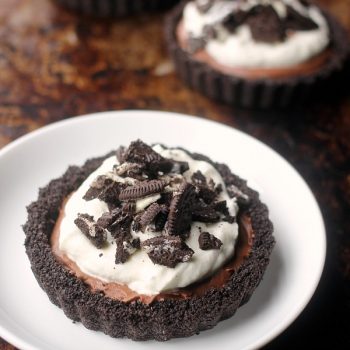 Oreo crusted tarts filled with chocolate mousse topped with whipped cream and crushed oreos