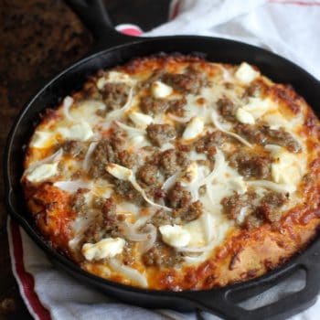 Baked pan pizza in the skillet topped with sausage and onion