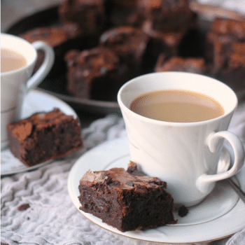 Super fudgy brownies cut for serving with a cup of coffee
