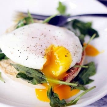 A runny poached egg on top of spinach and an english muffin