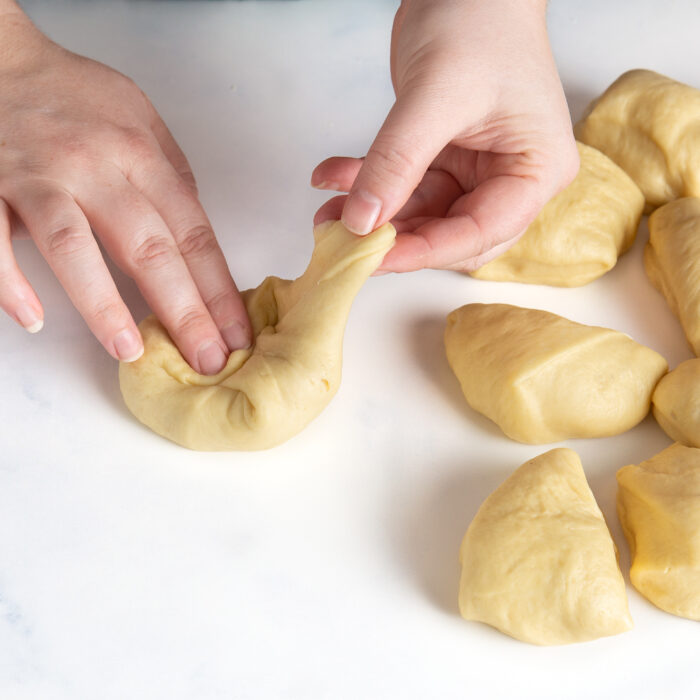 Shaping the rolls by pulling the seam of the dough ball into the center.