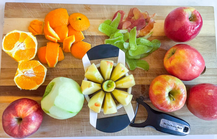 a cutting board with peeled apples, orange, and a knife