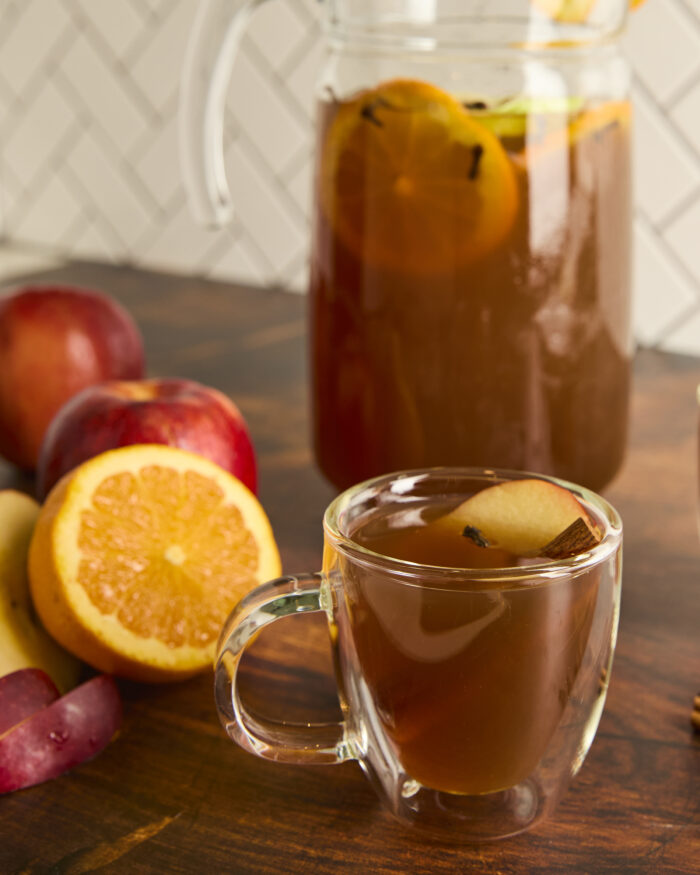 apple cider in a clear glass with cinnamon stick garnish and an apple slice