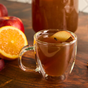 apple cider in a clear glass with cinnamon stick garnish and an apple slice