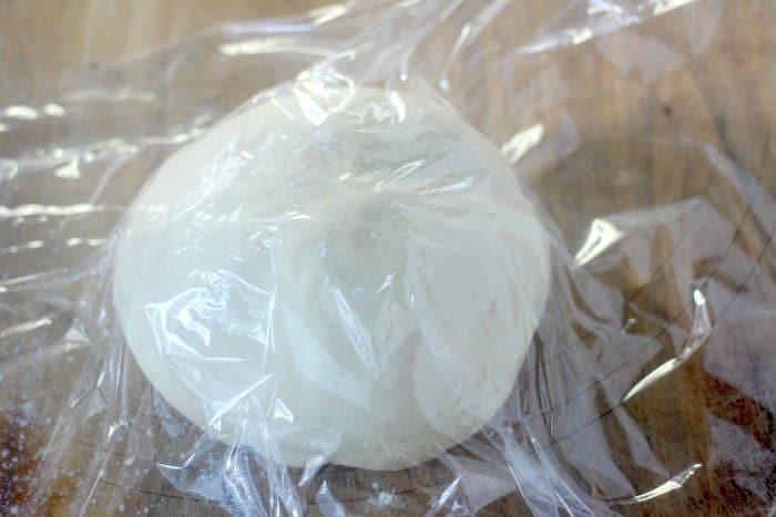 This easy pizza dough comes together in no time and is a "no rise" dough! This basic pizza dough will become a fast family favorite for homemade pizza night! Pizza dough ball resting with plastic wrap over top to relax gluten strands