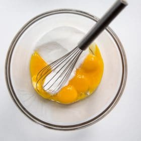 Egg yolks and sugar in a bowl with a whisk