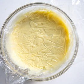 Pastry cream in bowl with plastic wrap over the top touching the cream