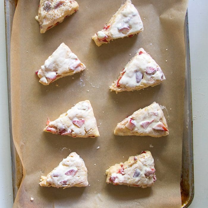 Unbaked strawberries and cream scones on a sheet pan brushed with cream ready to be baked