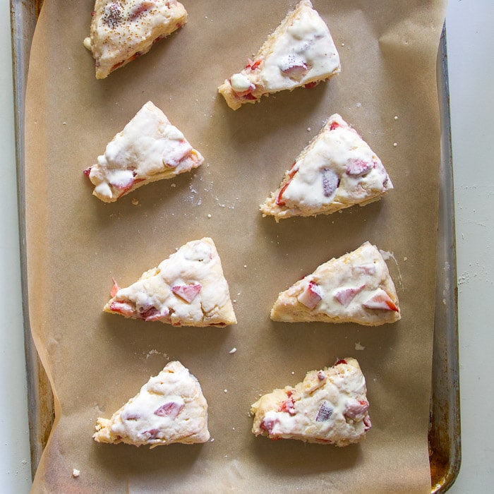 Unbaked strawberries and cream scones on a sheet pan brushed with cream ready to be baked