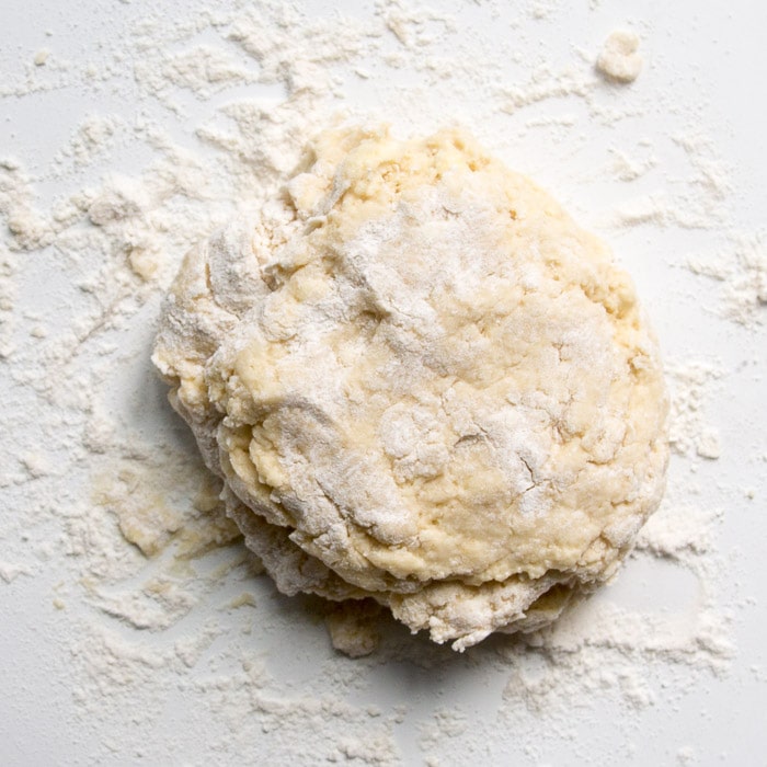 Learn the process of how to make lemon scones that are soft, fluffy, and moist! These lemon scones are tender and flavorful and topped with a tangy lemon glaze! Scone dough on a countertop being brought together in a ball