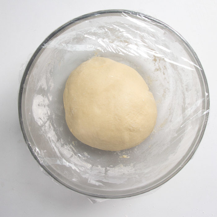 Dough in a bowl topped with plastic wrap bulk-fermenting