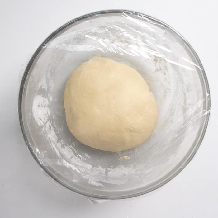 Kneaded dough ball in bowl wrapped in plastic wrap
