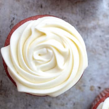 Cream cheese frosting piped into a rose design on top of a red velvet cupcake