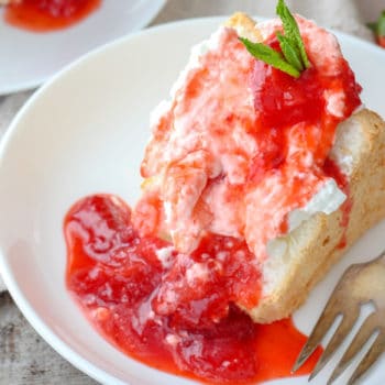 A slice of angel food cake topped with whip cream and fresh strawberry sauce with a mint sprig
