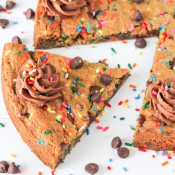 Chocolate Chip Cookie Cake with swirls of frosting on top with colorful sprinkles with a piece cut out